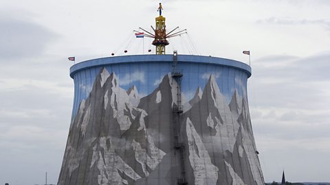 A view of the cooling tower at Wunderland Kalkar. It has mountains painted on it and a swinging merry-go-round is visible from the top