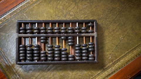 An antique abacus sits on a vintage green desk. An abacus is a frame with beads that slide along rods to perform arithmetic 