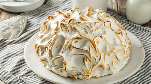 A Baked Alaska, perfectly toasted, on a white plate, on top of a stripy placemat