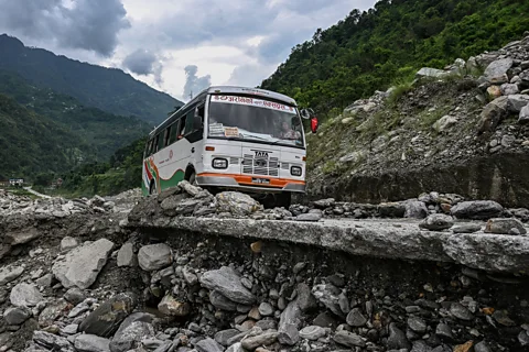 Getty Images A bus in Nepal picks its way along a road on a hillside that is crumbling away beneath the road (Credit: Getty Images)