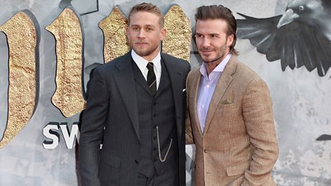 David Beckham in a light brown suit poses for a photo with Charlie Hunnam in a dark suit