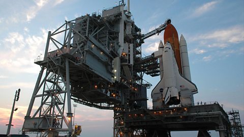 A NASA space shuttle, white and orange, surrounded by scaffolding