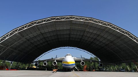 A large white aircraft with yellow and blue stripes representing the Ukranian flag sits in a domed airhanger 