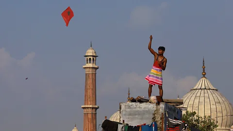 Vijay Pandey A man in a red vest and a colourful wrap around his waist standing on a roof top flying a red kite with the tower and dome of the Jama Masjid Mosque in Old Delhi in the background (Credit: Vijay Pandey)