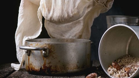 Process of making non-dairy almond milk - extraction of grain almond via white textile at vintage pan over old wooden table.