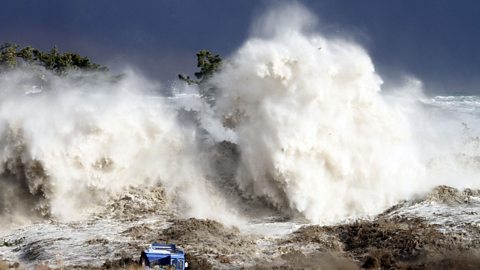 Huge tsunami waves are shown hitting a rocky coastal area