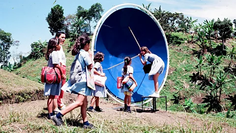 Gaviotas Children play in a large round blue dish device inside a white metal ring while others stand by (Credit: Gaviotas)