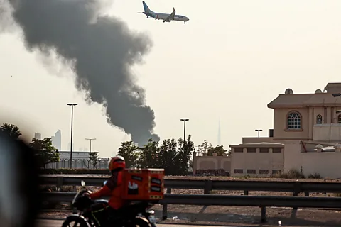 AFP via Getty Images An aircraft prepares for landing as a smoke plume rises from a fire near Dubai International Airport on 16 March (Credit: AFP via Getty Images)