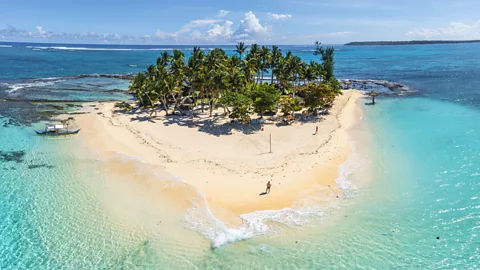 Getty Images Aerial view of a tiny tropical sand island surrounded by shallow turquoise water and lined with palm trees (Credit: Getty Images)