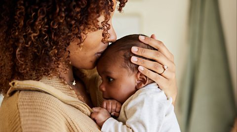 A close-up of a mother holding her baby close; she is placing a kiss to her head.