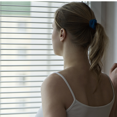 A woman staring through window blinds