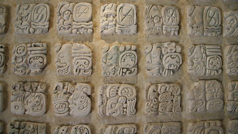 A stone wall covered with many small square carvings. Each square has a symbol carved into it. 