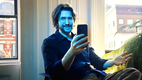 Hana Mendel The author Thomas Germain sits holding a smartphone, with blue light shining on him (Credit: Hana Mendel)