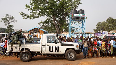 Rwandan peacekeeper soldiers from the United Nations in a UN truck beside a crowd of people.