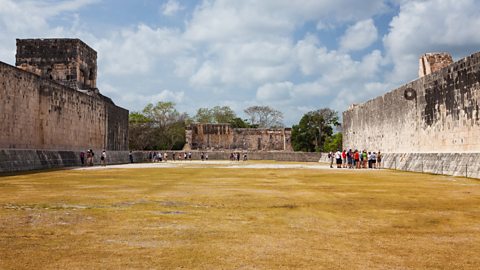 A grass pitz court with two large stone walls on either side. 