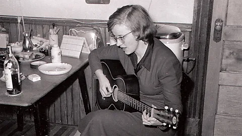 The Musick Group/ Heroic Cities LLC Black-and-white photo of Connie Converse sits a table playing guitar (Credit: The Musick Group / Heroic Cities LLC)