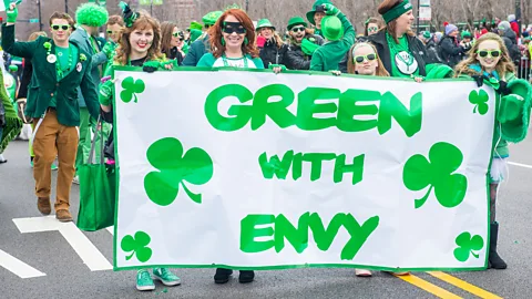 Alamy At a parade, four young women dressed in green hold a banner that reads "Green with Envy", with six clovers spaced around the words (Credit: Alamy)