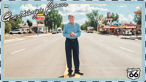 Johnny Kompar Angel Delgadillo stands in the middle of wide street on Route 66 in a postcard-style image reading "Greetings from Route 66" (Credit: Johnny Kompar)