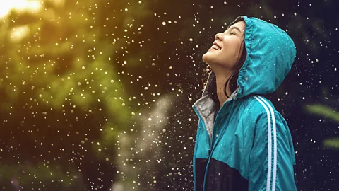 Getty Images A woman in a green sports jacket with the hood up smiles as she leans her head up, eyes closed, towards the falling rain (Credit: Getty Images)