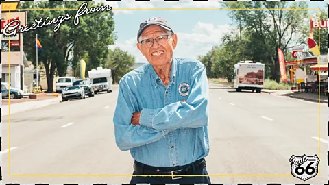 Johnny Kompar Angel Delgadillo stands in the middle of wide street on Route 66 in a postcard-style image reading "Greetings from Route 66" (Credit: Johnny Kompar)