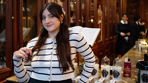 Hervé Lassïnce /BBC A young woman stands next to countertop with selection of perfumes at a vintage perfume shop (Credit: Hervé Lassïnce)
