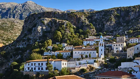 Getty Images Whitewashed buildings with terracotta roofs and a church bell tower on a mountainside on Albania's Adriatic Coast (Credit: Getty Images)
