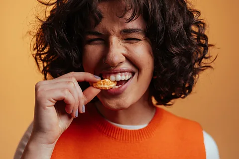 Getty Images A woman with dark curly hair biting down with enjoyment on an tangerine segment (Credit: Getty Images)