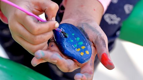child paints a pebble in bright colours