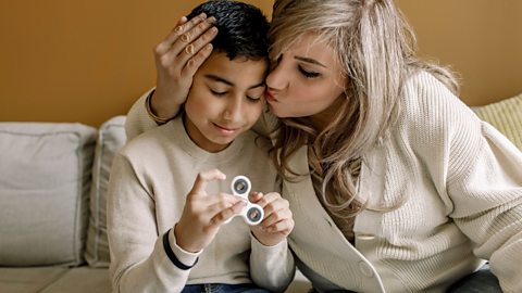 Child using a fidgit toy getting a hug from their mother.