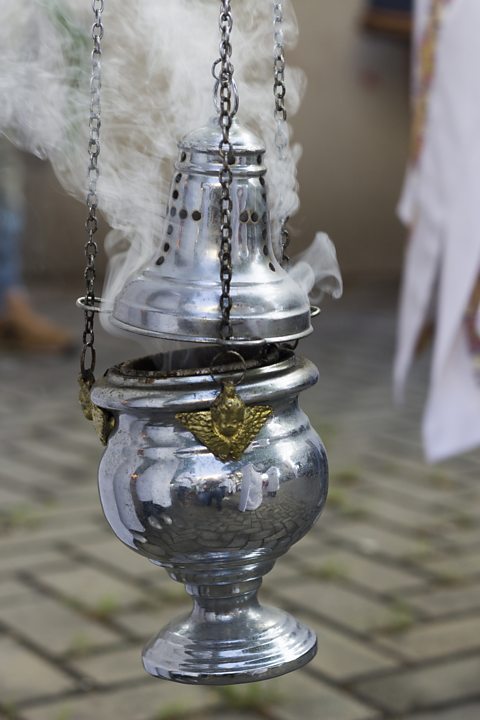 A polished silver incense burner suspended by chains, with a domed lid and small holes, releasing white smoke