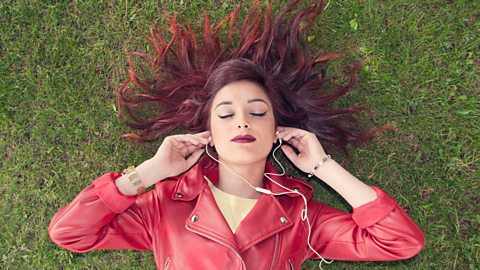 A person laying on the grass listening to a podcast.