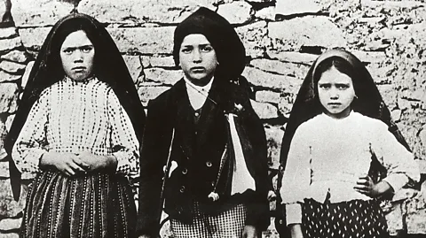 Getty Images A black-and-white photograph of three young girls stood against a dry stone wall (Credit: Getty Images)