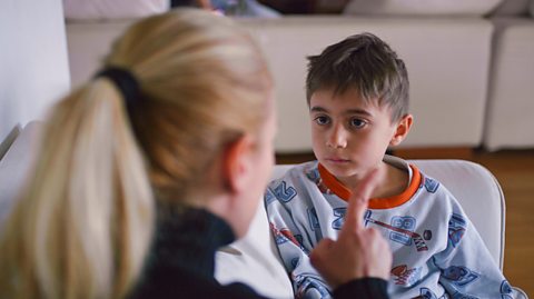 Mother tells off small boy on couch - pointing finger at him.