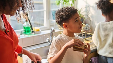 mum and two children at the sink - boy holds a sandwich