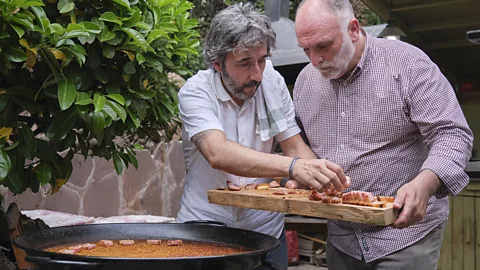 Courtesy of José Andrés and Family in Spain Two men hold a charcuterie board while standing next to a large paella pan (Credit: Courtesy of José Andrés and Family in Spain)