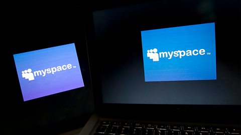 Two laptops in the dark. Both their screens are blue with the 'myspace' logo - white text with three people emojis