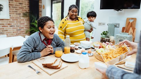 school boy looks excited at dinner table as mum and toddler look on