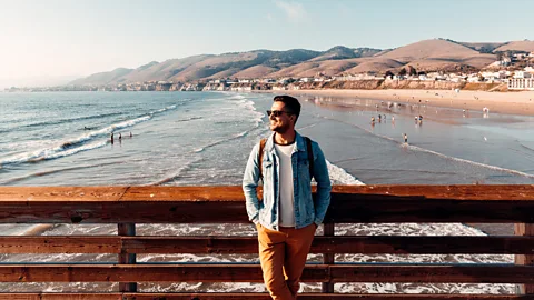 Getty Images Man leaning against pier fence with beach and coastline behind him at Pismo Beach, California (Credit: Getty Images)