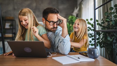 Stressed out Dad on a laptop, there are two children pestering him.