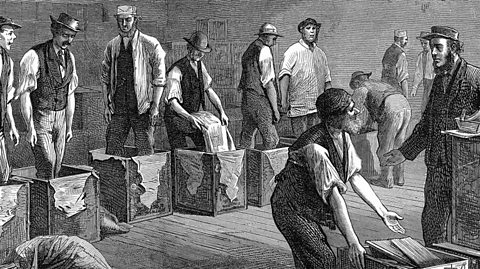A black and white artists impression of cargo being moved at East India Company - mean work and have boxes in front of them