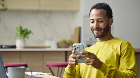 Getty Images A man sits staring at his phone and smiles at it (Credit: Getty Images)