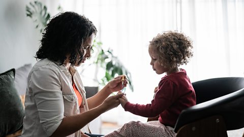 A woman paints a young girls' fingernails.