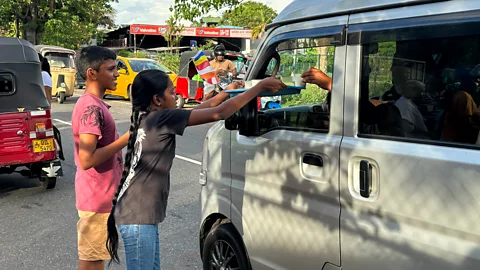 Zinara Rathnayake A young girl offers a tray of drinks through the window of a white van on a busy Colombo street during Vesak (Credit: Zinara Rathnayake)