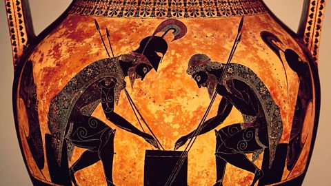 A close up image of an Ancient Greek vase depicting the fictional heroes Achilles and Ajax playing dice at a table. The background is orange and the figures are in black silhouettes. 