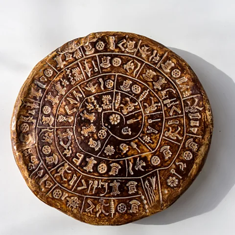 Getty Images The symbols on the 4,000-year-old Phaistos disc – found in the remains of a Minoan palace on Crete – remain largely undeciphered (Credit: Getty Images)