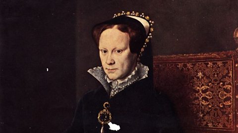 A portrait of Queen Mary I, who has a serious expression. She is wearing dark clothes, a headdress and is sat against a dark background.