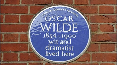 On a brick wall is a circle blue plaque for author and poet Oscar Wilde. It reads 'London County Council, Oscar Wilde, 1854-1900, wit and dramatist lived here' in white text