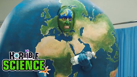 A person dressed as an Earth character holds a plastic bottle. 