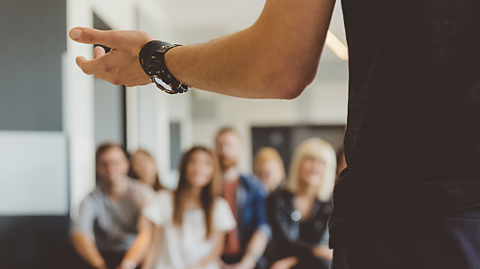 Image of a young person's arm - they are giving a speech to a small group of peers.