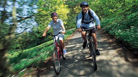 An image of two teenage boys cycling down a country lane. Both are wearing bike helmets